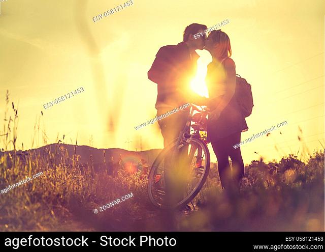 Young couple with bike is kissing on a field, sundown