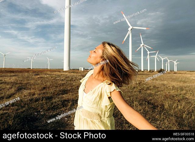 Carefree woman enjoying in front of wind turbines at field