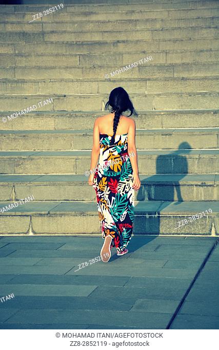 Rear view of a young woman wearing a summer dress walking up the stairs outdoors
