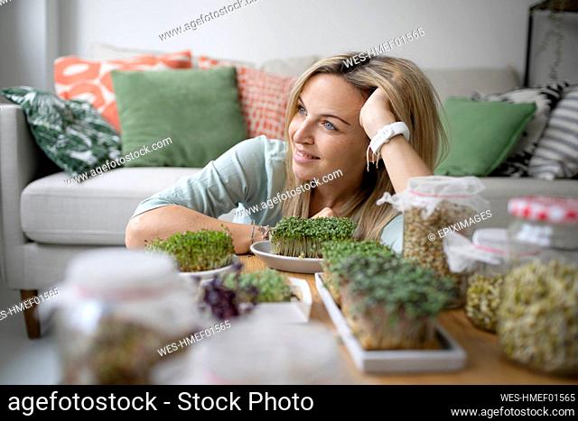 Thoughtful woman with head in hand sitting by homegrown saplings at home
