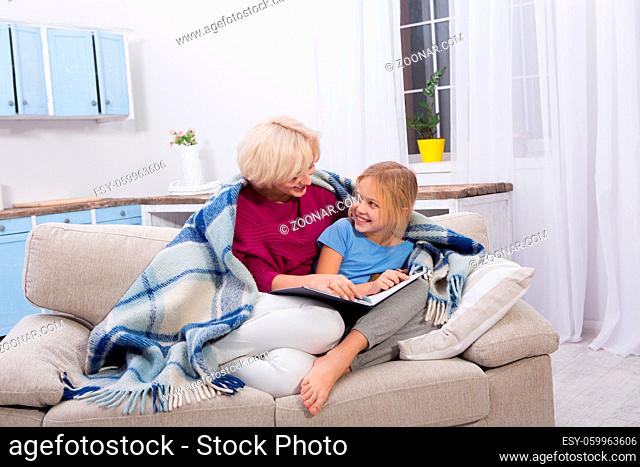Smiling mom and her sick daughter staying at home, reading books. Mother taking care of her child while illness