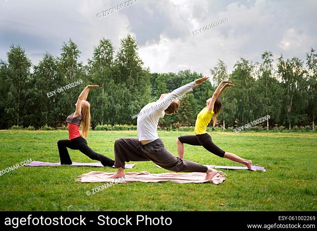 Training in park - instructor shows flexibility exercise for group of girls in park, early morning