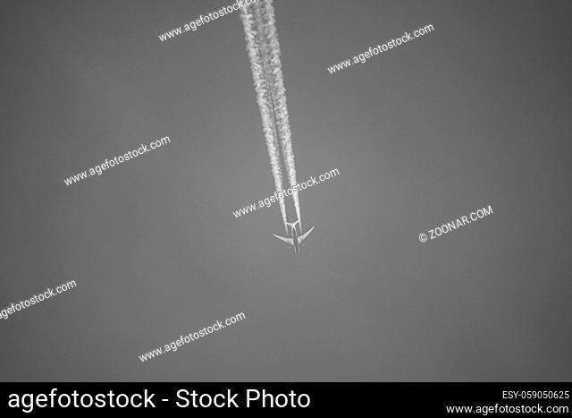 a large passenger aircraft flies in the cloudless blue sky and produces a white glowing condensation trail