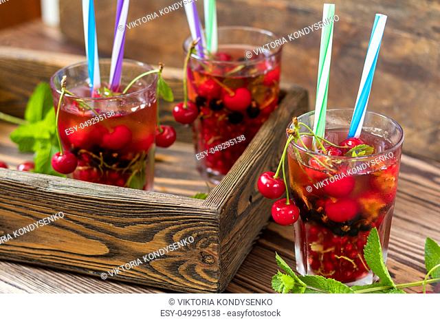 Three glasses of refreshing drink flavored with fresh fruit in wooden box surrounded by fruit. Wooden background