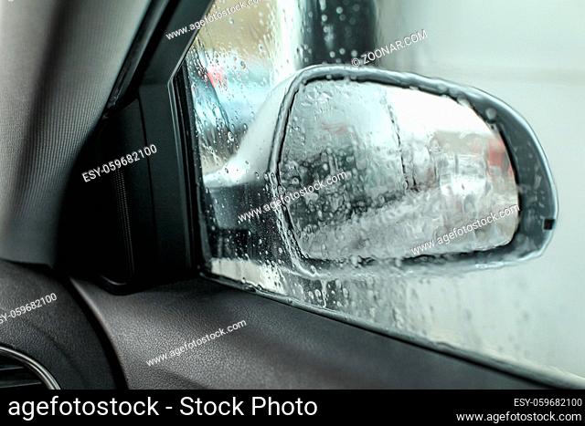 View from inside the car, looking at side mirror, wet from water and soap when being washed in carwash