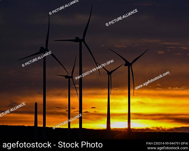 14 March 2023, Brandenburg, Jacobsdorf: Colorful clouds glow in the early morning sunrise over the landscape with several wind turbines