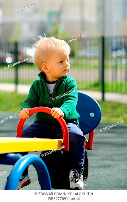 Portrait of toddler child outdoors. One year old baby boy wearing green sweater at playground seesaw