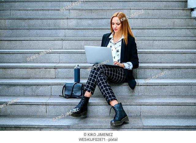Young businesswoman sitting on stairs using laptop