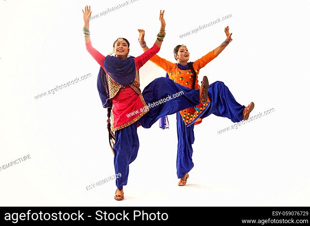 Two Giddha Dancers performing a dance step with hands up and a leg uplifted