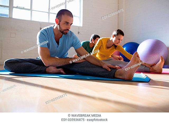Yoga instructor with students stretching legs at club