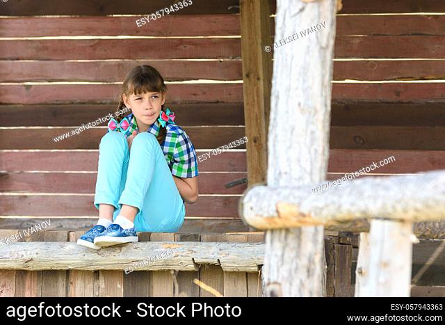 A ten-year-old girl sits in a wooden gazebo and looks thoughtfully into the distance