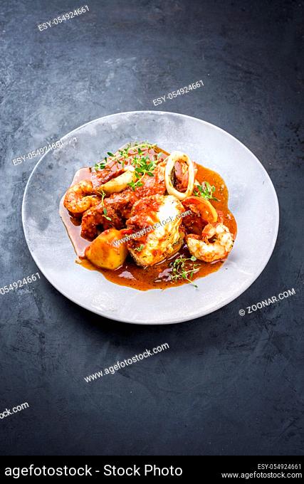 Traditional Brazilian fish stew moqueca capixaba with fish filet and king prawns in tomato sauce as closeup on a modern design plate