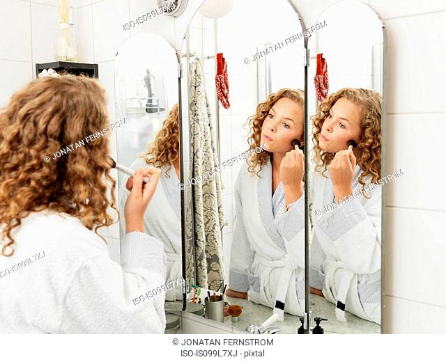 Young woman applying make-up in mirror