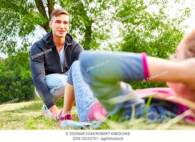 Frau im Workout macht Sit-ups und Mann hilft bei der Fitness Übung