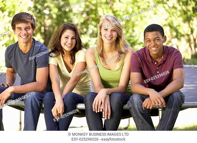 Four Teenage Friends Sitting On Trampoline In Garden