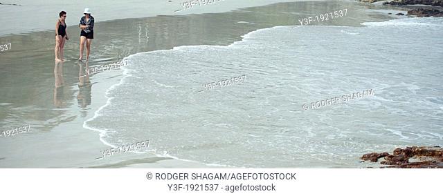 Two women stroll on the beach at the edge of an incoming tide
