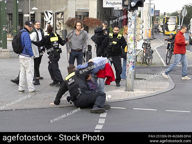 06 October 2023, Berlin: A police officer prevents activists from the climate protection group Last Generation from sticking to the streets at Potsdamer Platz