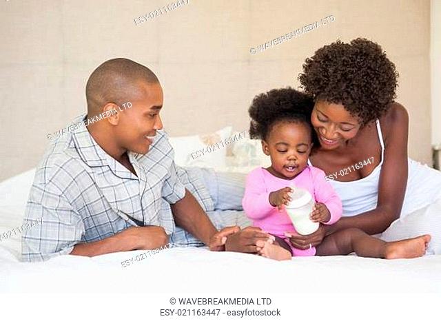 Happy parents and baby girl sitting on bed together