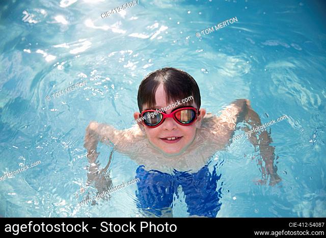 Portrait smiling boy in goggles swimming in sunny swimming pool
