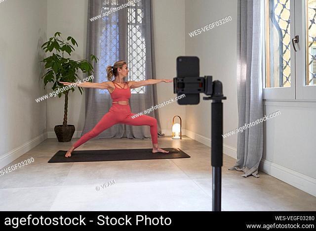 Female yoga instructor filming herself on mobile phone for online lessons in exercise room