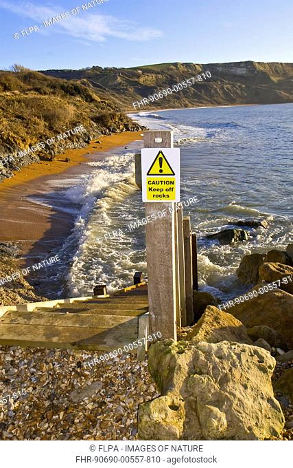 'Caution, Keep off rocks' sign attached to post beside wooden steps leading to beach, Ringstead Bay, Dorset, England, January