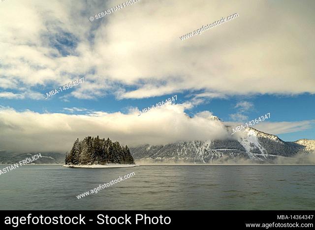 The small island of Sassau in Walchensee in the Byrian Alps covered with snow with clouds in winter