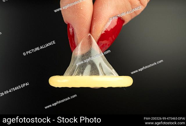 25 March 2020, North Rhine-Westphalia, Bielefeld: A condom is held with two fingers. The strict contact requirements in the public due to the Corona crisis are...