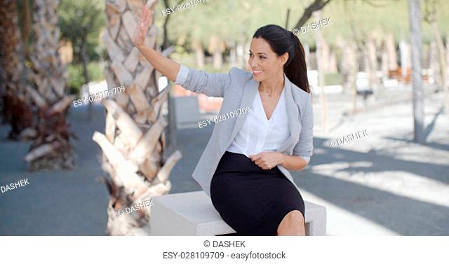Stylish young woman in an urban park standing alongside a tropical palm tree holding the lapels of her jacket as she looks to the side