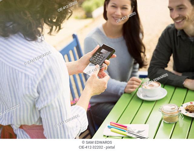 Couple watching waitress using credit card reader at outdoor cafe