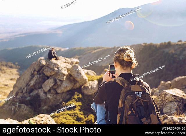 Young woman photographing male friend sitting on top of mountain