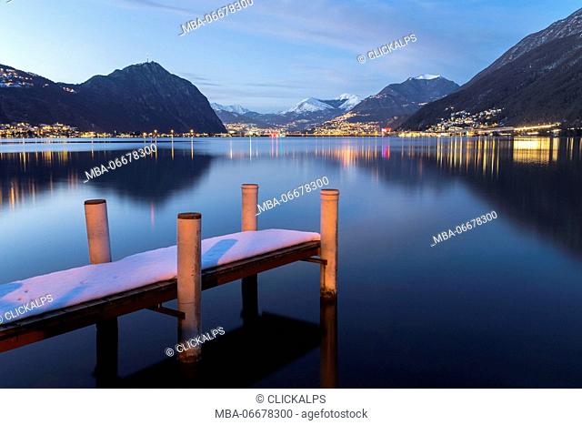 Evening lights of Lugano and Campione d'Italia in front of a pier on Lake Ceresio, Riva San Vitale, Canton Ticino, Switzerland