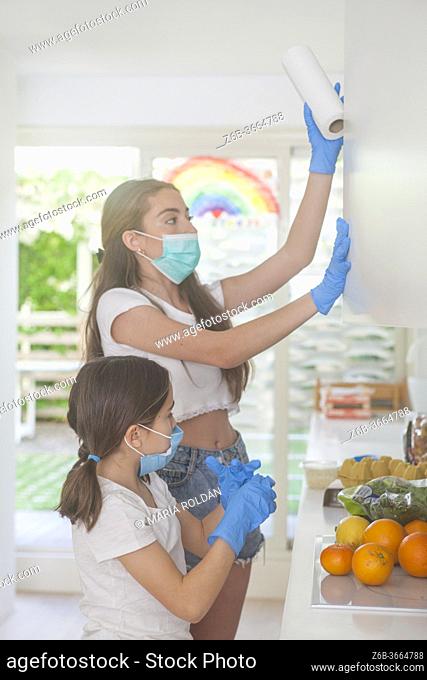 mother and daughter with masks and gloves in kitchen
