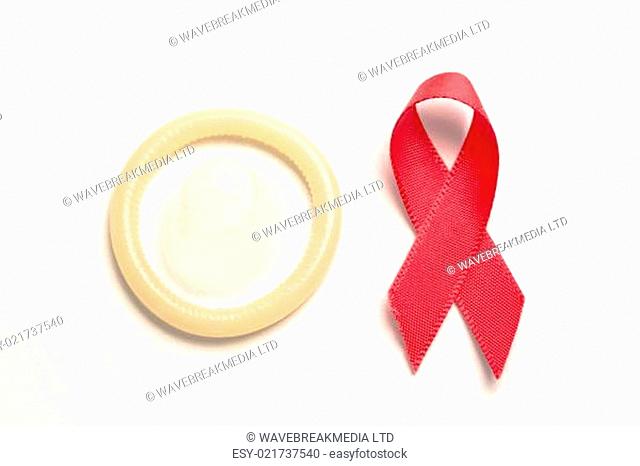 Red awareness ribbon and condom on white background