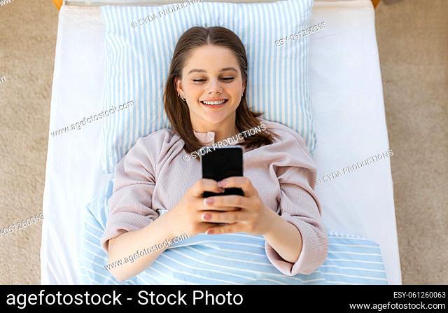 happy girl with smartphone in bed at home