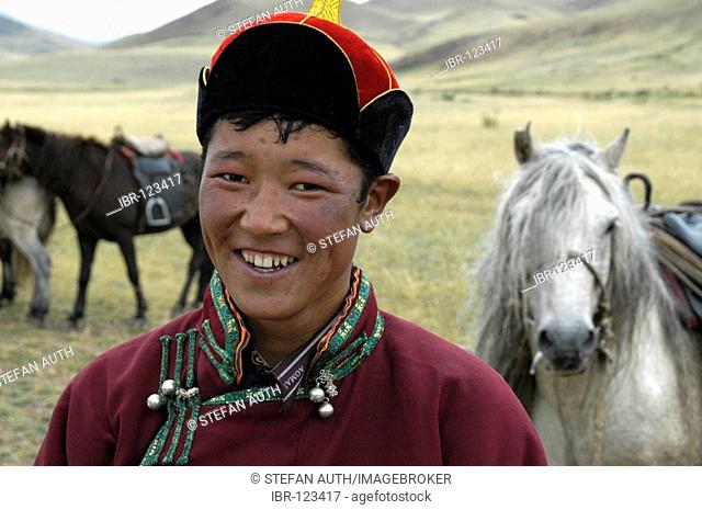 Portrait nomads shepherd boy dressed in traditional coat and hat in front of his horse in the steppe Kharkhiraa Mongolian Altai near Ulaangom Uvs Aymag Mongolia