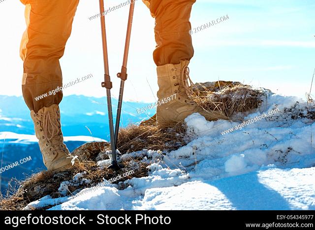 Close-up of a tourist's foot in trekking boots with sticks for Nordic walking standing on a rock stone in the caucasian mountains