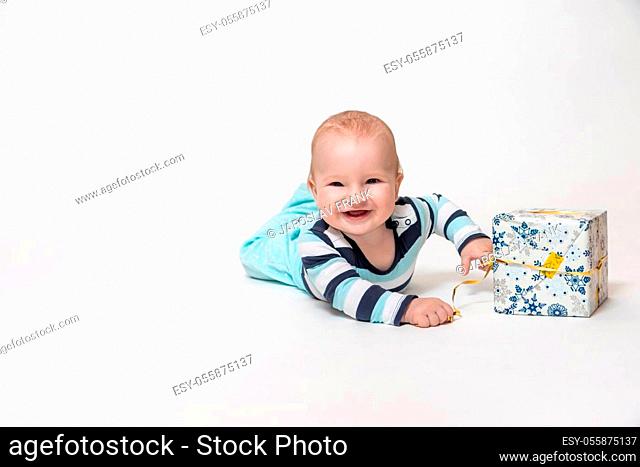 Smiling toddler boy is holding Christmas package lying on the floor. All is on the white background