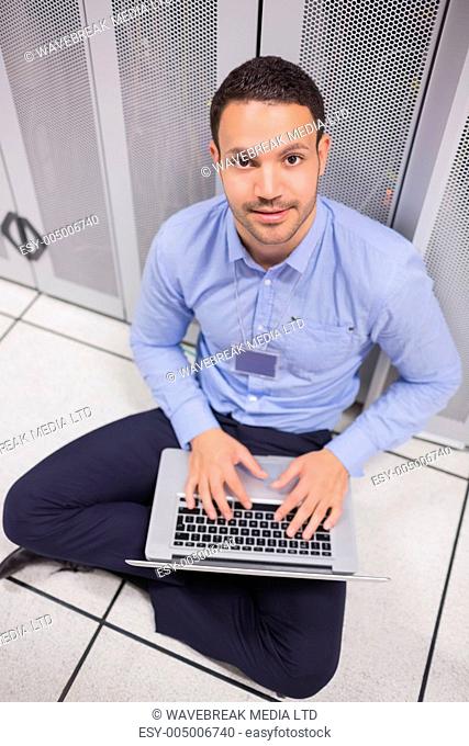 Smiling man using laptop in front of servers of data center