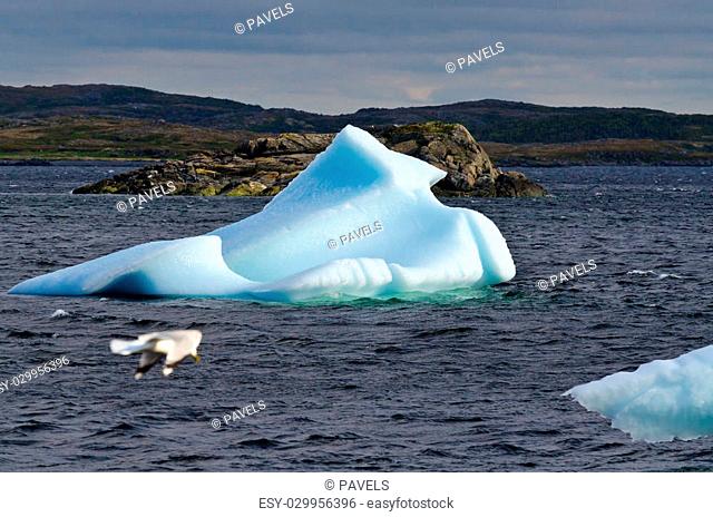 Bright white iceberg on dark water and rock background