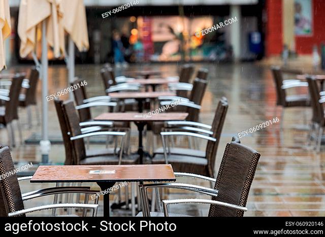 Empty and wet tables and chairs of closed outdoor sitting area of cafeteria in city center on rainy day