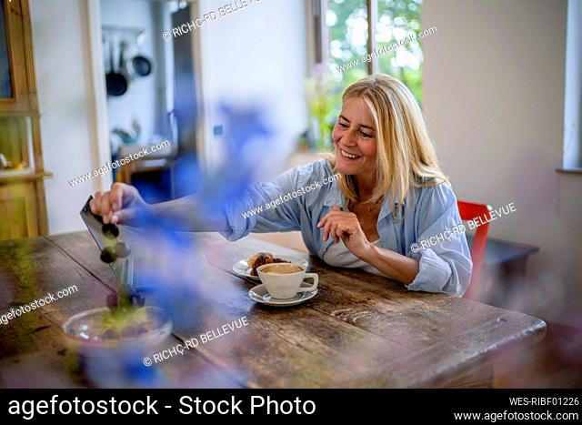 Happy mature woman eating fruit sitting by table at home