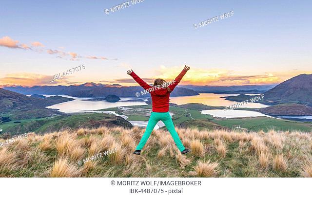 Hiker jumping with limbs spread out in the air, view of Lake Wanaka and mountains, sunset, Rocky Peak, Glendhu Bay, Otago, Southland, New Zealand