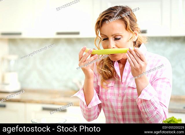 woman holds and tastes fresh green celery in the kitchen
