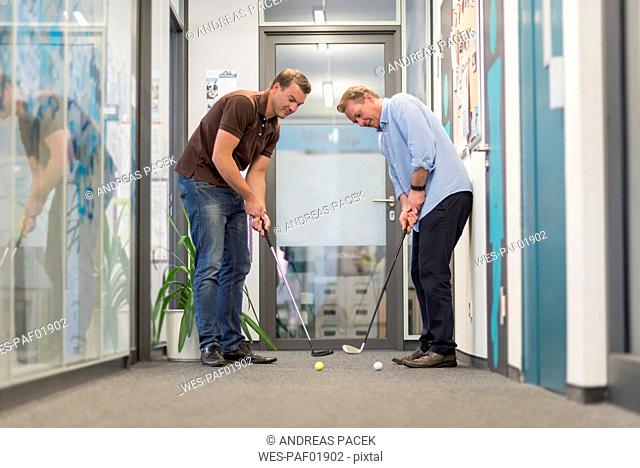 Two businessmen playing golf in office