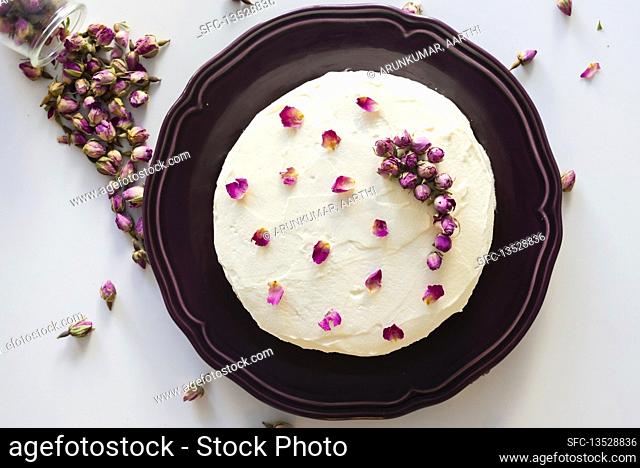 Rose cake decorated with dried rose buds and petals on a purple plate