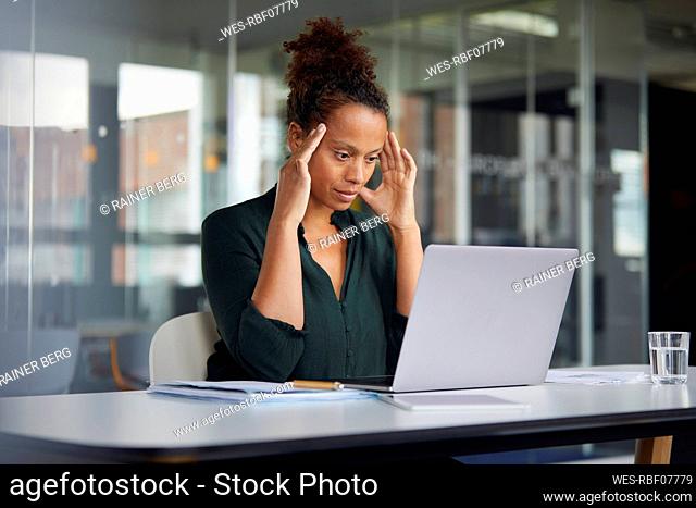 Portrait of pensive businesswoman at desk looking at laptop