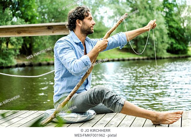 Man sitting on platform at the waterside with selfmade fishing rod