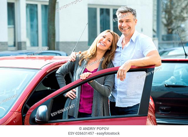 Portrait Of Happy Couple Standing With Their Newly Purchased Red Car