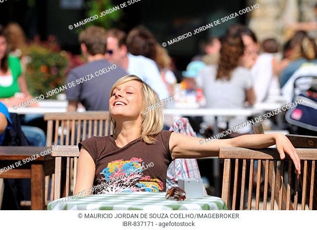 Young blonde woman sitting in a cafe, sunning herself, happy, relaxed, summer