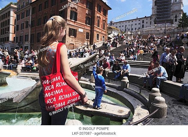 Young woman with a red Roma bag at Fontana della Barcaccia on Piazza di Spagna, Spanish Steps in background, Rome, Italy